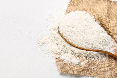 Tahta kaşık, beyaz arka planda un ve buğday kulakları.