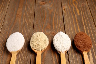 Farklı türde un ve kakao içeren tahta kaşıklar kahverengi ahşap arka planda.