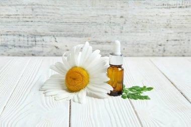 Bir şişe temel yağ ve papatya çiçeği açık ahşap masada.