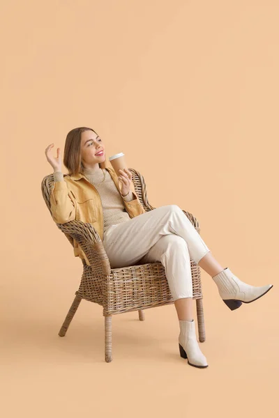 坐在米色背景的柳条椅上喝咖啡的年轻女人 — 图库照片