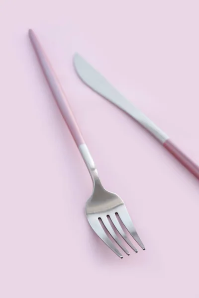 ピンクの背景にステンレス製のフォークとナイフ — ストック写真