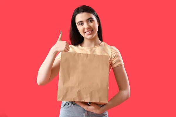 赤い背景に親指アップを示す寿司の紙袋を持つ若い女性 — ストック写真