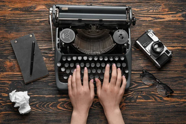 Vrouw Typend Schrijfmachine Met Bril Notitieboekje Camera Bruine Houten Ondergrond — Stockfoto