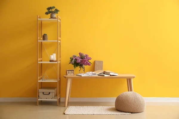 stock image Interior of room with lilac flowers in vase, table and shelving unit