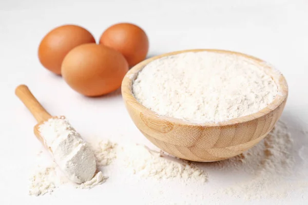 stock image Wooden bowl with wheat flour, scoop and eggs on white background