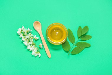 Akasya çiçekli bir kase bal ve yeşil arka planda kaşık.