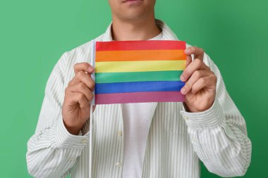 Yeşil arka planda LGBT bayrağı olan genç adam, yakın plan.