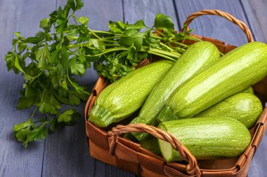 Mavi ahşap arka planda yeşil kabaklı ve maydanozlu sepet.