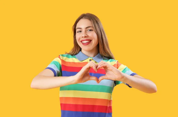 若いです女性で虹シャツ作る心で手で黄色の背景 — ストック写真