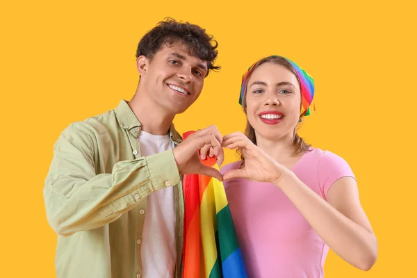 Lgbtの旗を持つ若いカップルが黄色の背景に心を作る — ストック写真