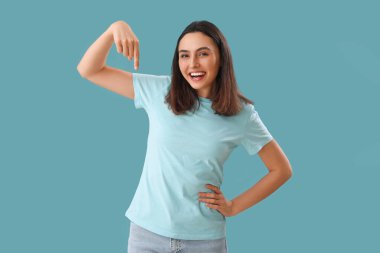 Genç bir kadın mavi arka plandaki bir şeyi işaret ediyor.