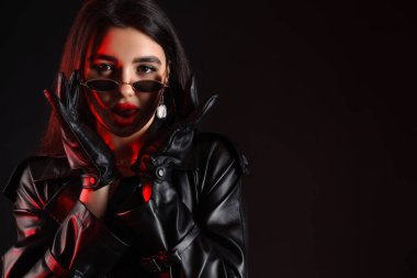 Güneş gözlüklü çekici bir genç kadın ve siyah arka planda deri eldivenler, yakın plan.