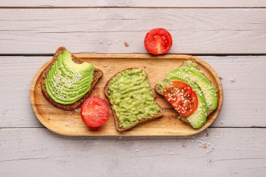 Hafif ahşap arka planda lezzetli avokado tostları.