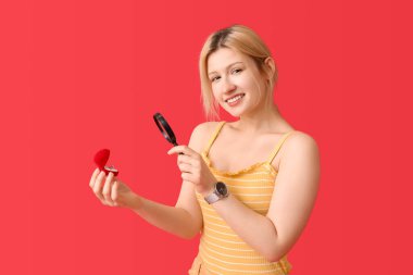 Kırmızı arka planda büyüteç ve nişan yüzüğü olan genç bir kadın.