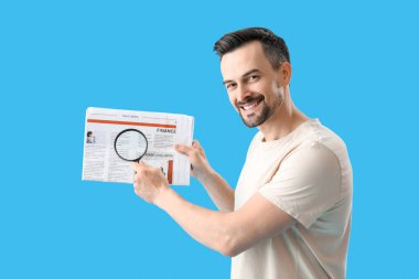 Büyüteci ve mavi arka planda gazetesi olan yakışıklı bir adam.