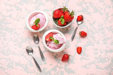Bir kase çilekli dondurma ve arka planda kaşıklar.