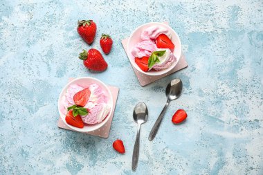 Bir kase çilekli dondurma ve arka planda kaşıklar.