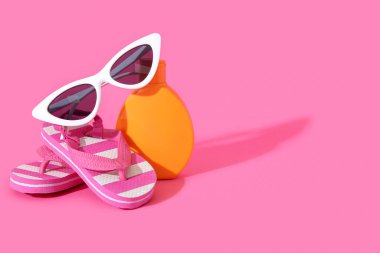 Güneş gözlüklü bir şişe krem ve pembe arka planda parmak arası terlik.