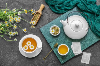 Siyah arka planda bir fincan sıcak papatya çayı, çaydanlık ve bal.