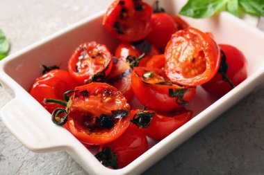 Lezzetli ızgara domatesli fırın yemeği ve gri arka planda fesleğen