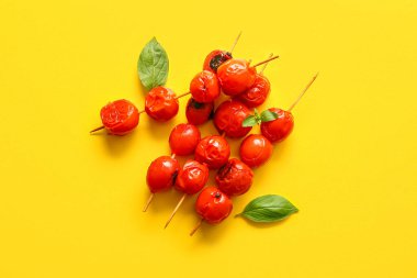 Lezzetli ızgara domatesli şişler ve sarı arka planda fesleğen.