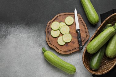 Gri arka planda taze yeşil kabaklı dilimler ve hasır çanak.