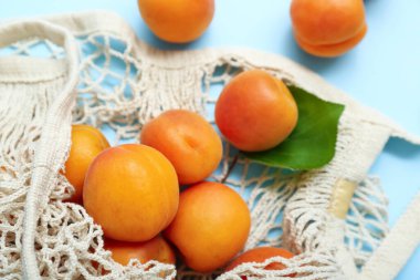 Taze kayısıları ve mavi arka planda yaprağı olan bir ip torbası.