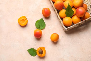 Bej arka planda taze kayısılarla dolu bir hasır kutu.