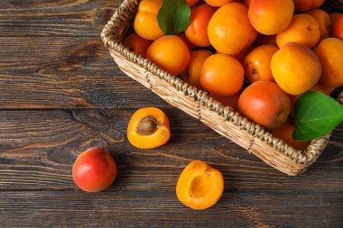 Ahşap arka planda taze kayısılarla dolu bir hasır kutu.