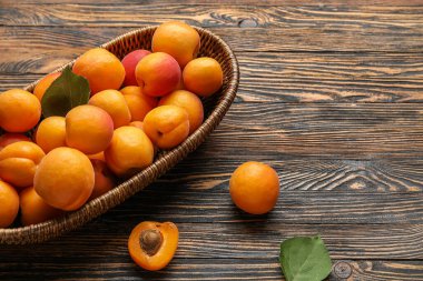 Ahşap arka planda taze kayısıları olan hasır bir kase.