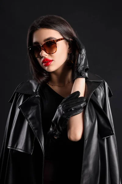 黒を背景にサングラスや革の手袋でスタイリッシュな若い女性 — ストック写真