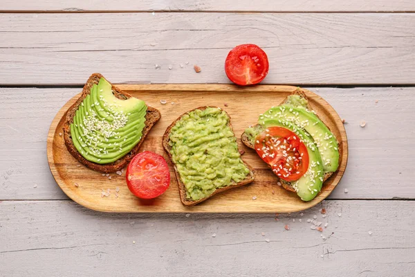 Hafif ahşap arka planda lezzetli avokado tostları.