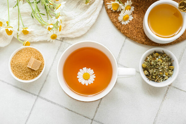 Cup of hot chamomile tea and honey on white tile background