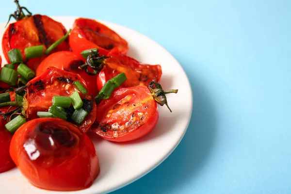 stock image Plate with tasty grilled tomatoes and green onion on blue background