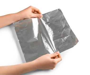 Beyaz arka planda alüminyum folyo tabakası olan kadın elleri, yakın plan