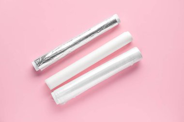 Alüminyum folyo ruloları, fırın kağıdı ve pembe arka planda yemek filmi.