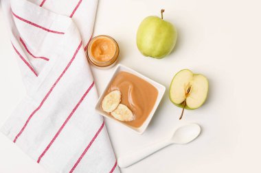 Bir kase sağlıklı bebek püresi ve beyaz arka planda taze elmalar.
