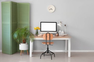 Modern bilgisayar ve ışık duvarının yanında narsist çiçekleri olan şık bir iş yeri.