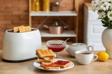 Modern tost makinesi, tatlı reçelli tost ve mutfaktaki masada bir fincan çay.