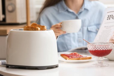Kadın, modern tost makinesi ve lezzetli reçelli tostlarla kahvaltı yapıyor.