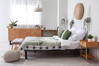 Konforlu yatak odası, ahşap dolap ve sallanan ev bitkileri.