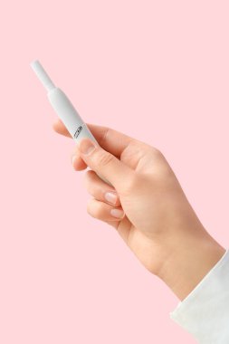 Kadın eli pembe arka planda modern elektronik puro tutuyor.