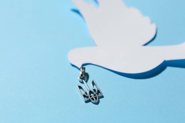 Mavi arka planda Ukrayna armalı kolye ve kağıt güvercin, yakın plan.