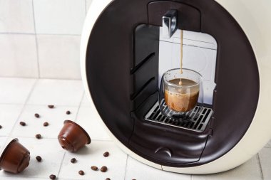 Damlayan espresso, fincan, kapsül kahve makinesi ve beyaz masa üzerinde fasulye.