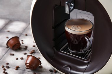 Gri grunge masasında bir fincan espresso, kozalar ve fasulye ile modern kapsül kahve makinesi.