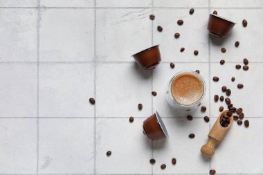 Bir fincan nefis espresso, kapsüller ve fasulyeler beyaz fayanslı masada.