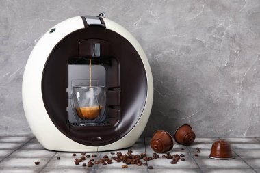 Damlayan espresso, fincan, kapsül kahve makinesi ve gri grunge masasında fasulye.