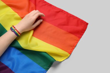 Gri arkaplanda gökkuşağı bilekliği ve LGBT bayrağı olan kadın eli