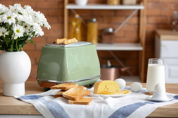 stock image Modern toaster with crispy bread slices, glass of milk, cheese and eggs on table in kitchen