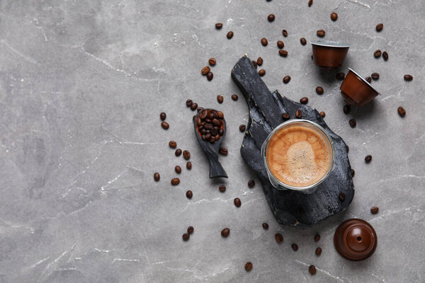 Slate board with cup of delicious espresso, beans and capsules on grey grunge table